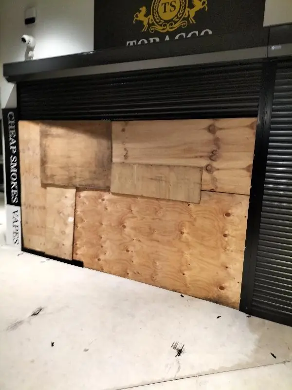 Storefront glass frontage boarded up with plywood after break-in damage, roller door down